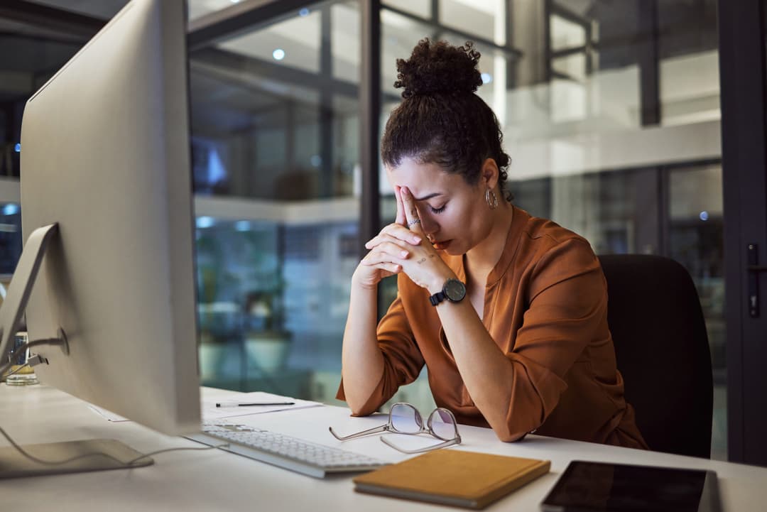 Women stressed at work with her head in her hands and eyes closed.