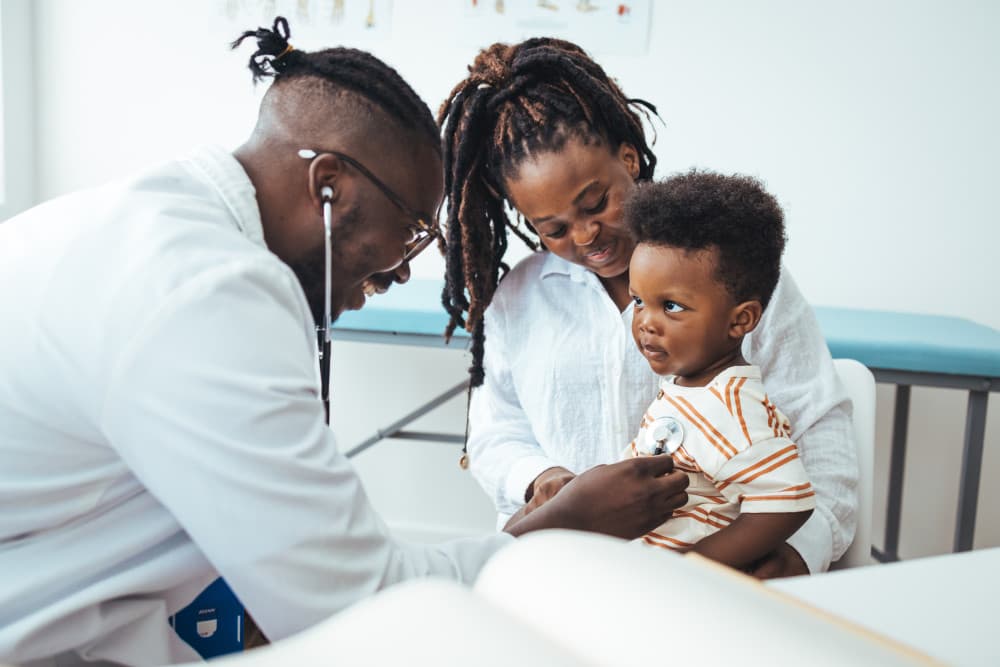 A happy toddler boy sits in his mother' lap at the pediatrician