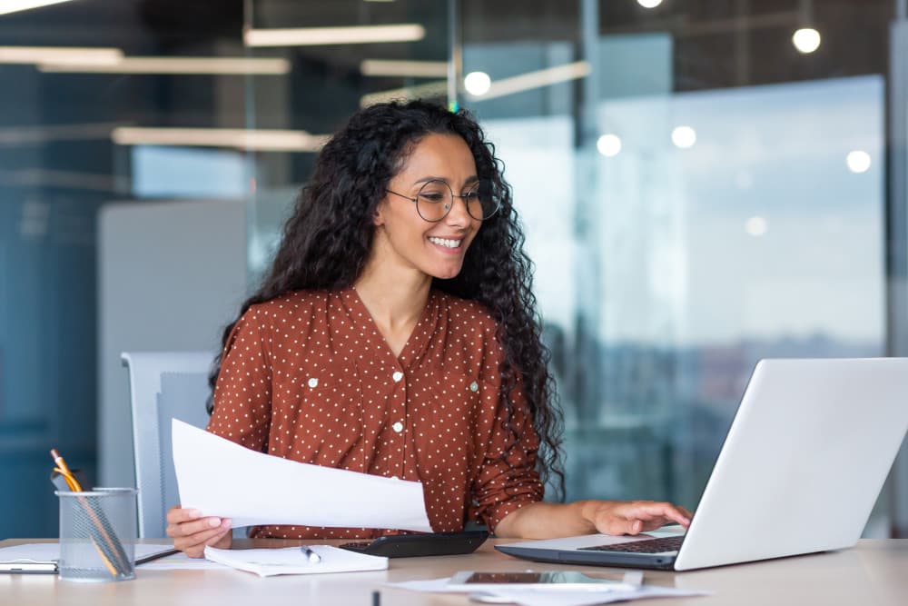 Young latin american businesswoman working inside office with documents and laptop