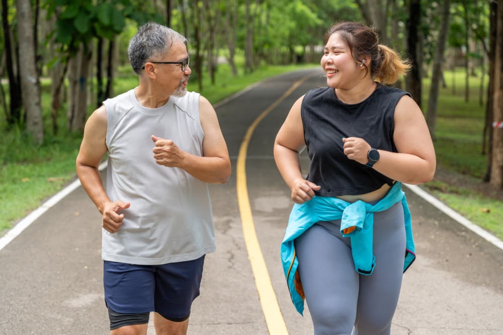 Happy middle age man and young overweight woman enjoy talking to each other during their morning run at running track of a local park