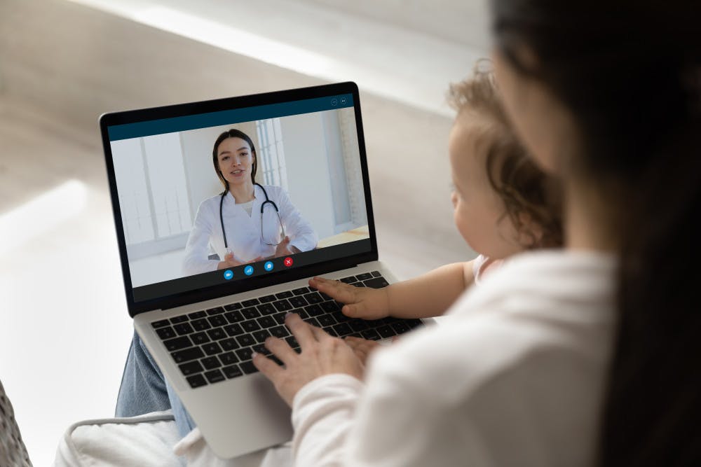 Young pediatrician giving consultation to new mom from laptop screen