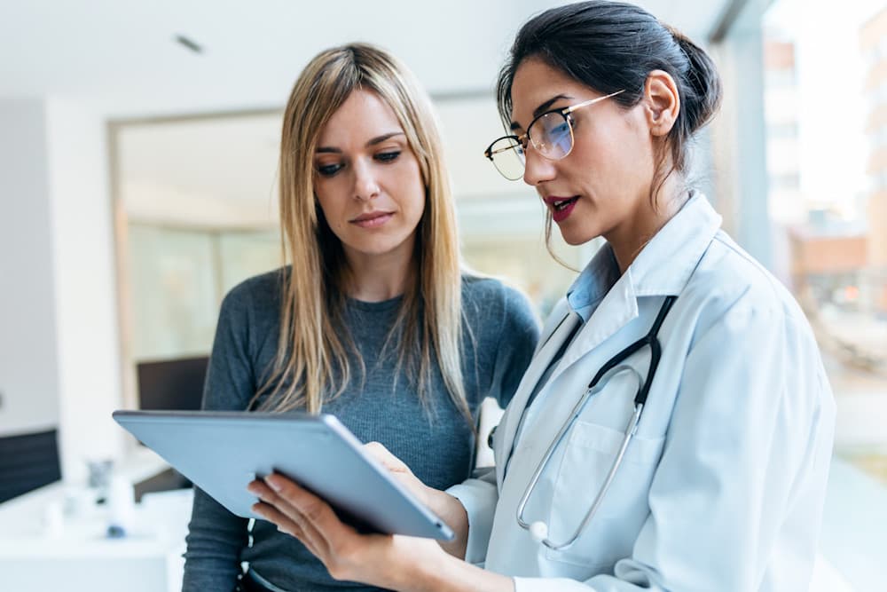 Doctor talking while explaining medical treatment with digital tablet to patient.