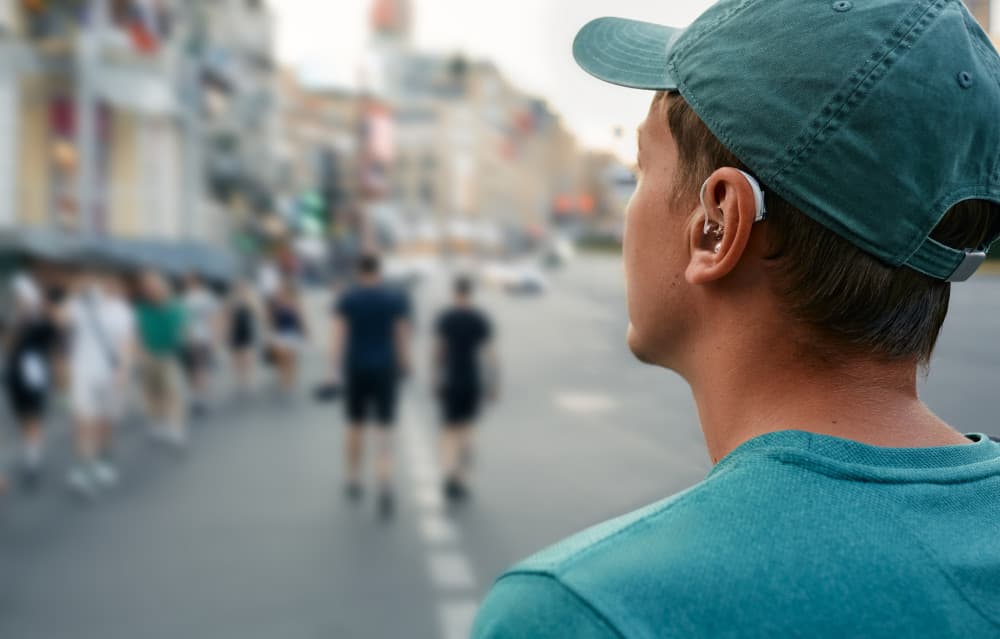 Young man with a hearing aid behind the ear in a noisy city hears people around well