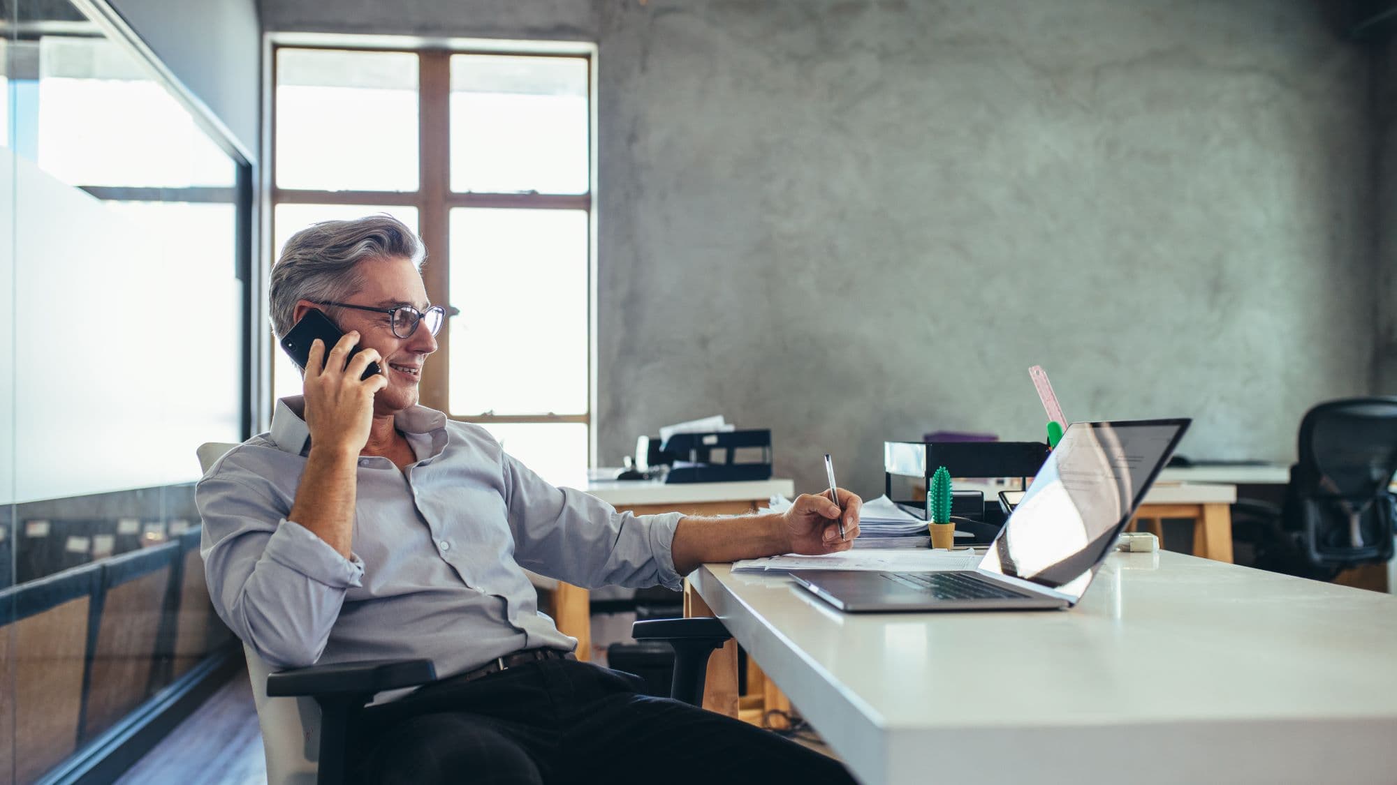 Male health insurance broker sitting at his desk discussing the risks and rewards of the Curative health plan over the phone and smiling