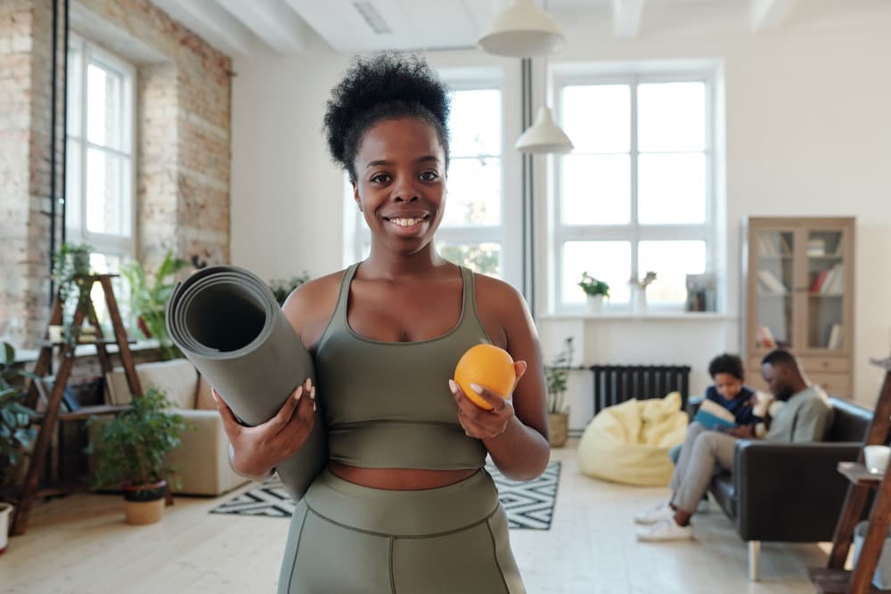 Healthy young woman smiling holding rolled mat and orange