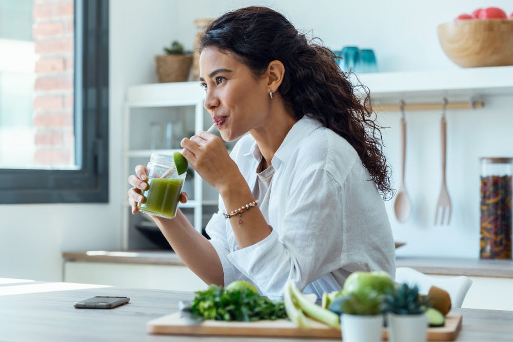 woman looking to sideways while drinking fruit detox juice in the kitchen at home.